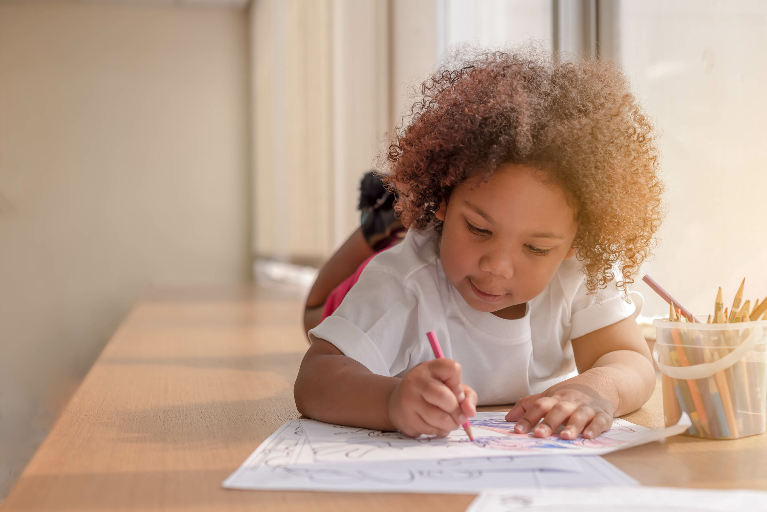 Little toddler girl laying down concentrate on drawing.  Mix Afr